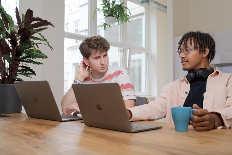 Two men seated at a table, each using a laptop, engaged in a discussion about account planning in Salesforce.